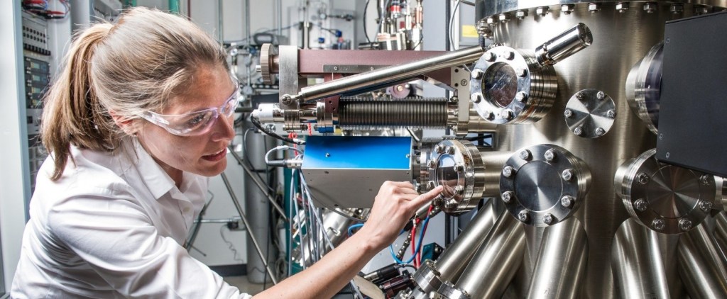 Una mujer con gafas de protección realiza tareas de mantenimiento en una compleja maquinaria de un edificio.